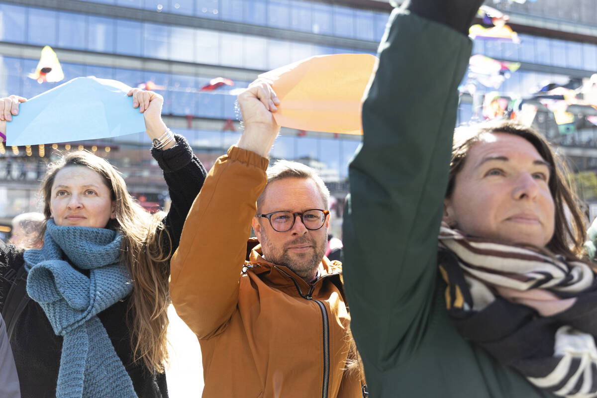 Tre vuxna som håller upp lappar i en manifestation