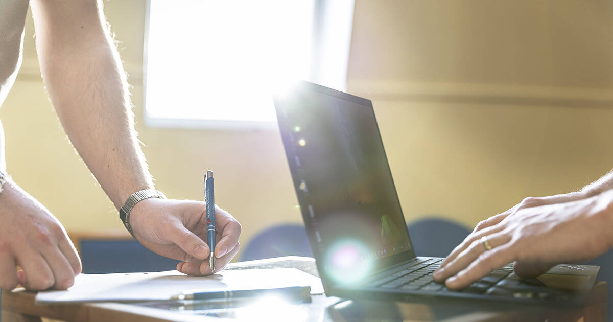 Händer, papper, penna och laptop