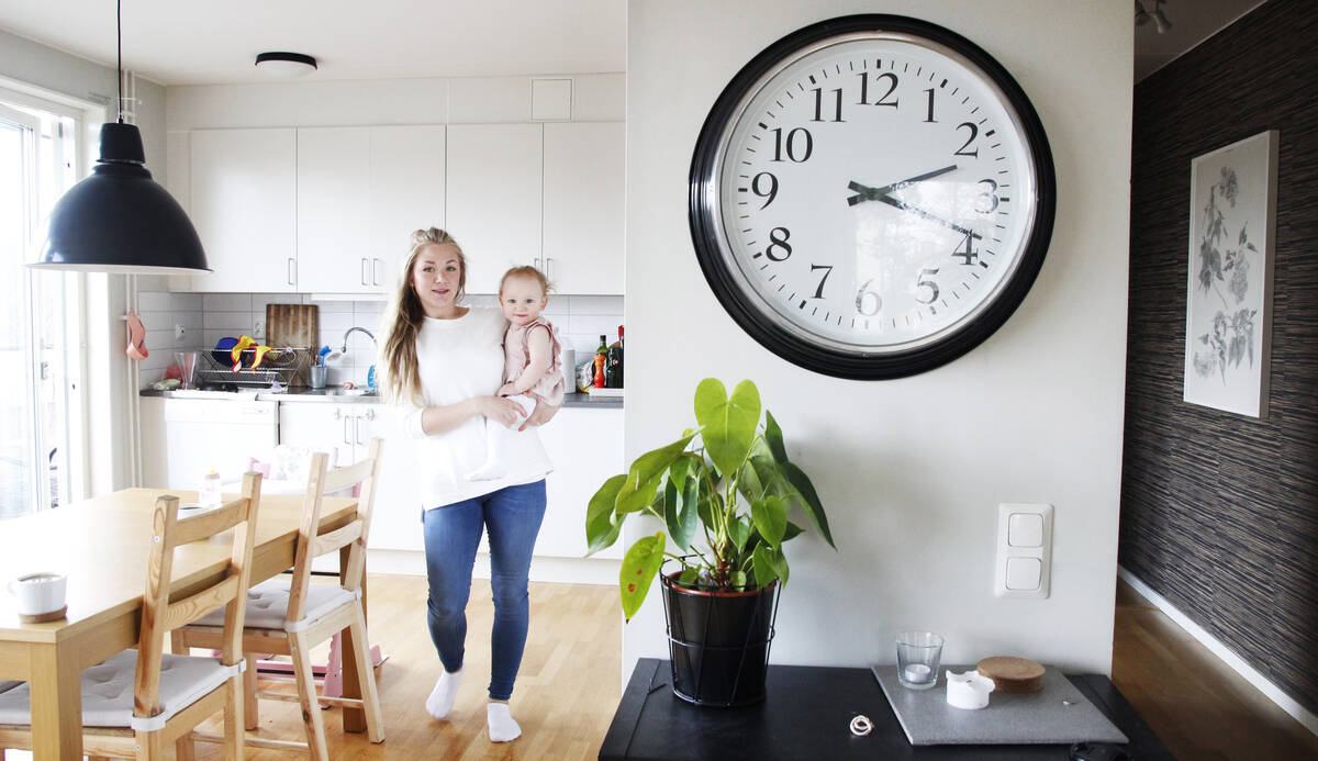 En ung glad mamma med bebis hemma i sitt kök.
