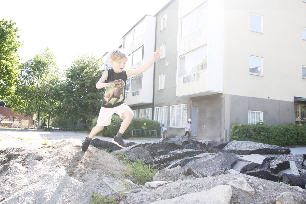 En liten sommarpojke leker i en grus- och asfaltshög i en förort.