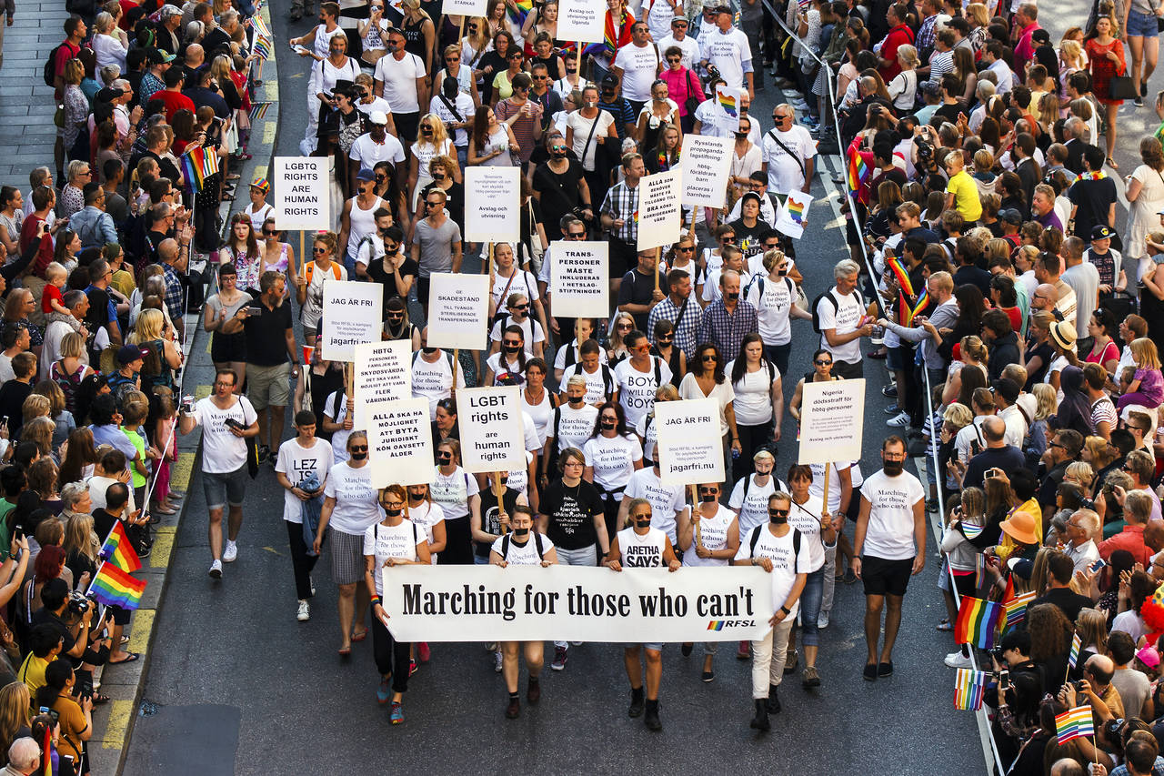 Sektionen Marching for those who can't bär banderollen synligt. En del har tejpat över sina munnar med svart tejp. Vid sidan av paradvägen står många människor och tittar på. Många regnbågsfalggor i luften.
