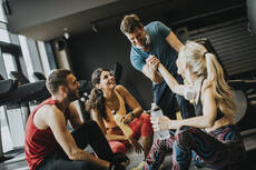 mp31310482-friends-in-sportswear-talking-and-laughing-together-while-sitting-on-the-floor-of-a-gym-after-a-workout.jpg